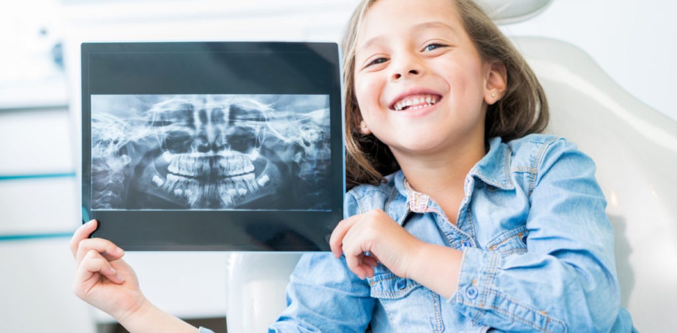 Girl at the dentist holding and x-ray and looking at the camera smiling